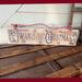 A handmade Christmas sign. Old time writing has been wood-burned onto a piece of reclaimed wood. Reindeer and holly are on either side. 